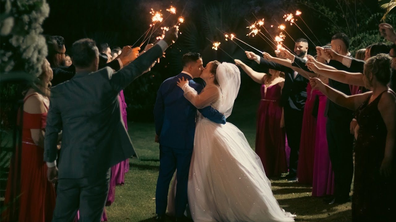 Noivos se beijando entre os convidados, com fogos de mão acesos